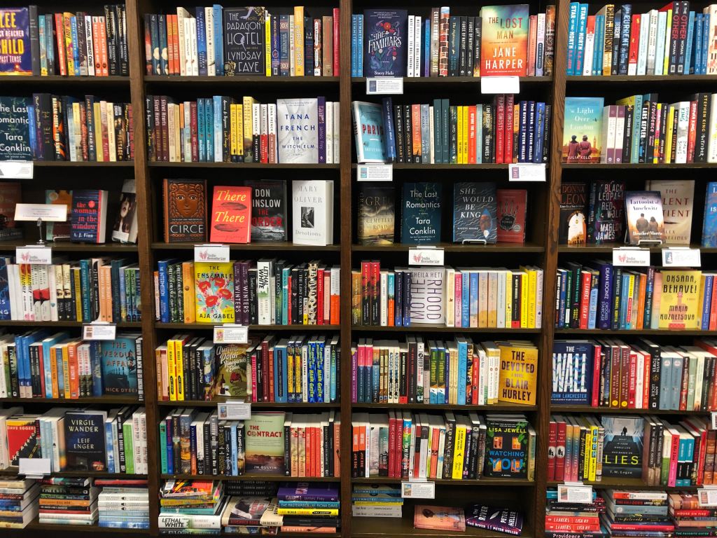 A bookshelf completely full of books fills the image. None of the titles or spines are legible, but the books are a range of colours and appear to be mostly novels.]